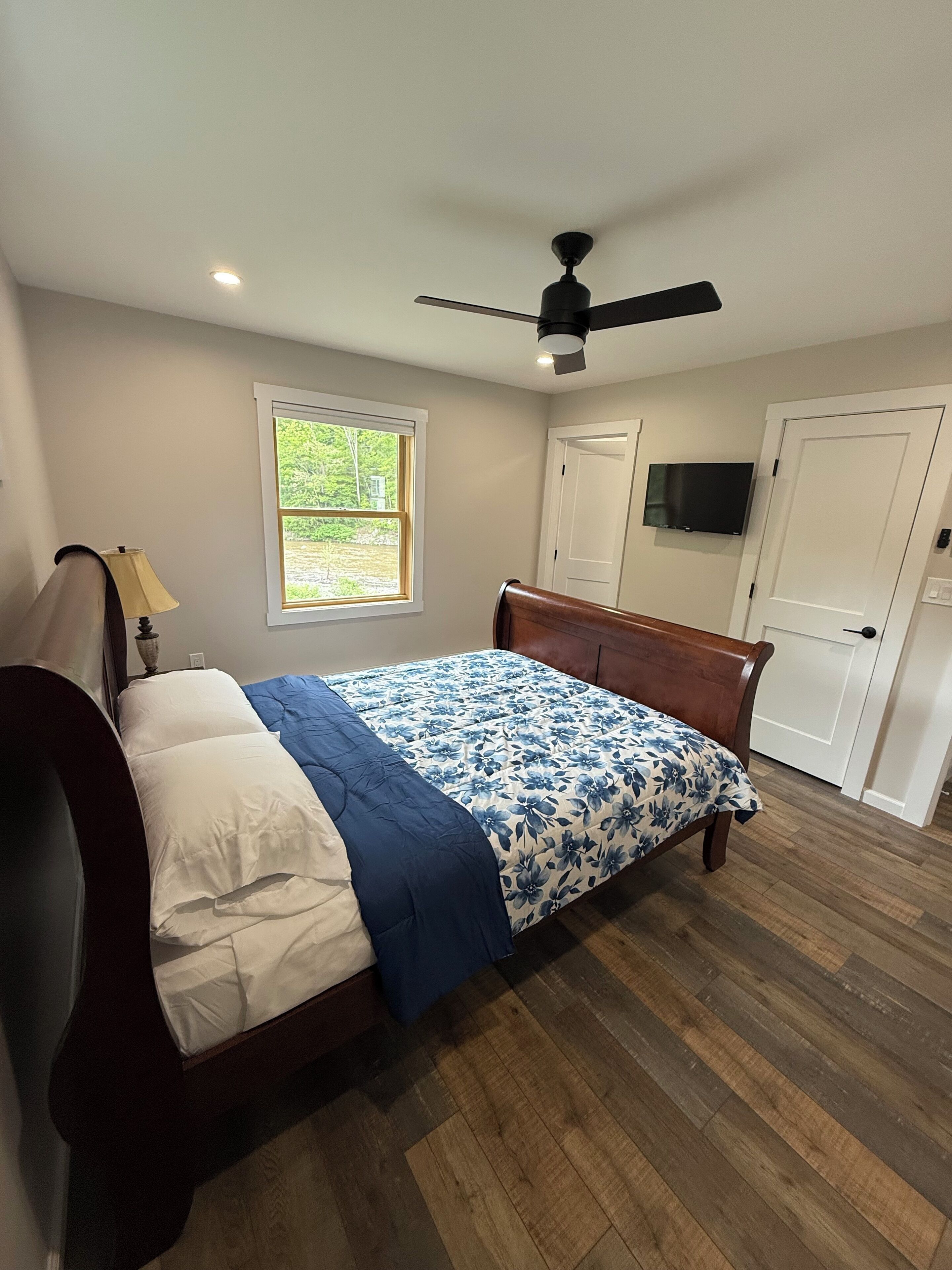 A bedroom with a bed, a ceiling fan, a window, and a door.