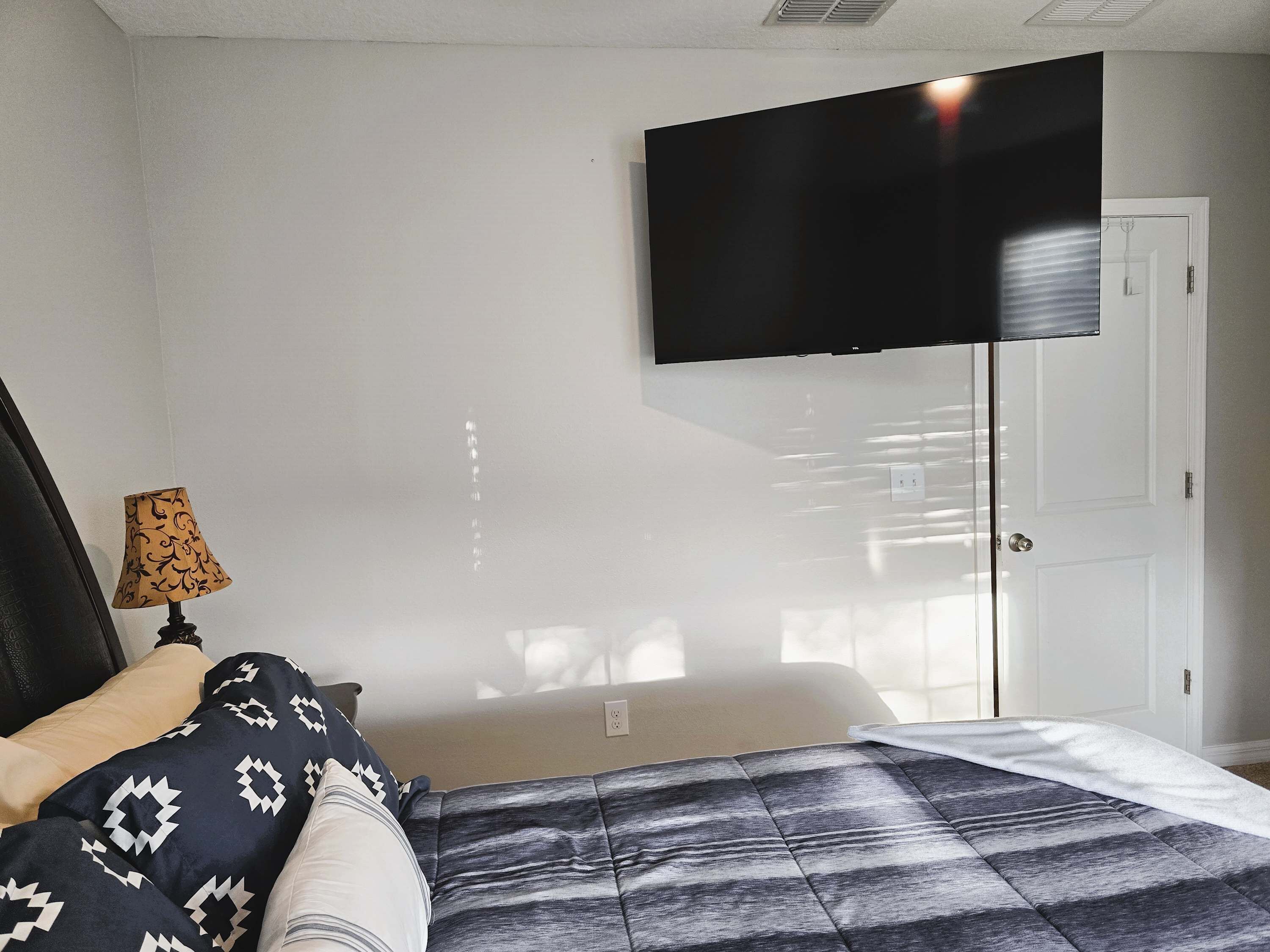 Un dormitorio con una cama, un televisor en la pared y una puerta.