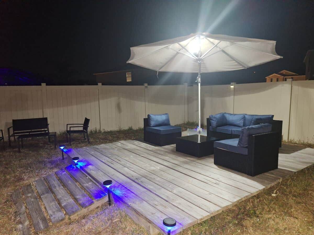 Eine Terrasse im Freien mit Holzdeck, zwei dunklen Sofas, einer Bank und einem Sonnenschirm.