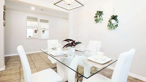 Un espace de salle à manger moderne avec une table en verre, des chaises blanches et un lustre aux motifs géométriques.