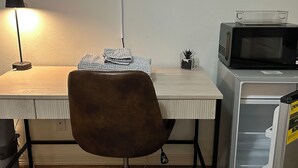Ein kompakter Arbeitsbereich mit Schreibtisch, einem braunen Stuhl, einer Lampe, einer Mikrowelle und einem kleinen Schrank.
