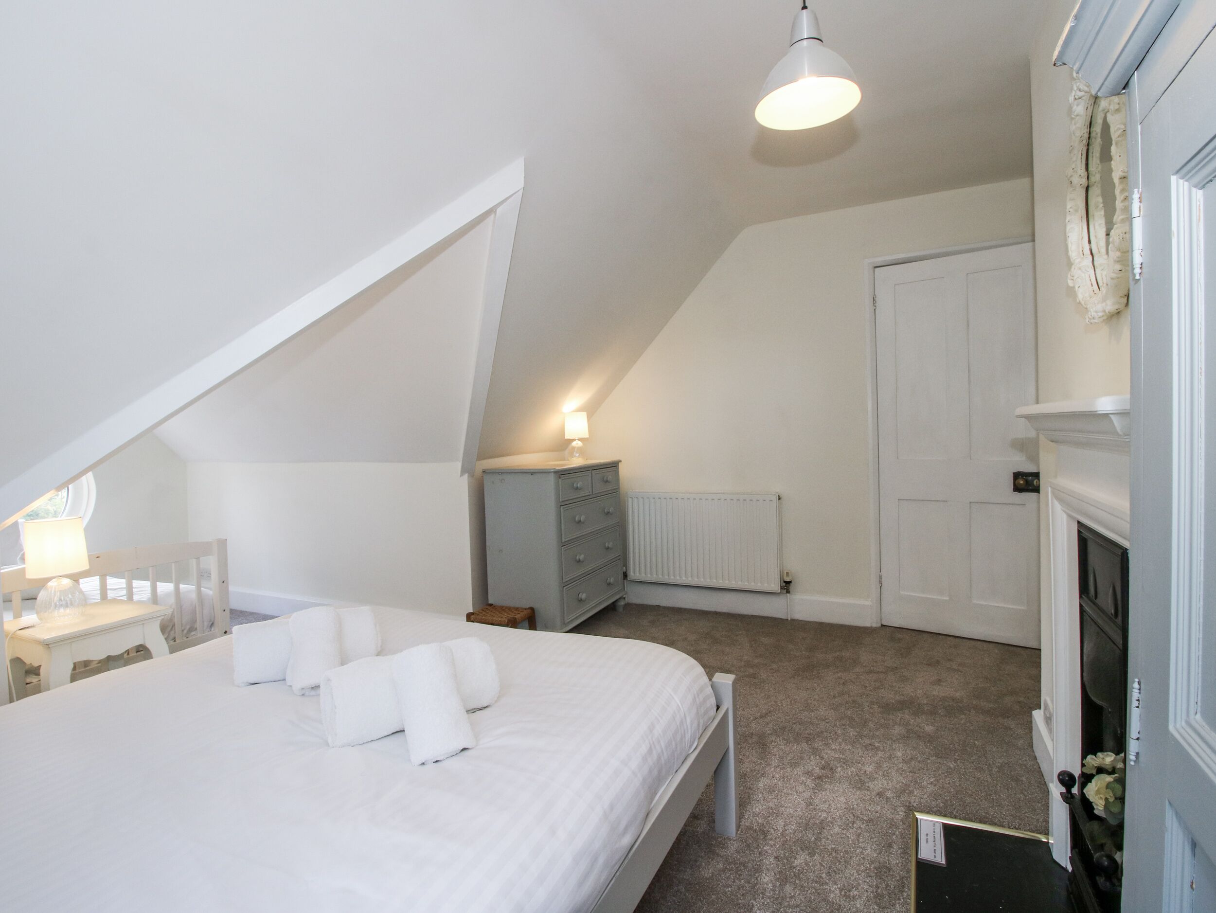 A bedroom with a bed, a dresser, a radiator, and a fireplace.