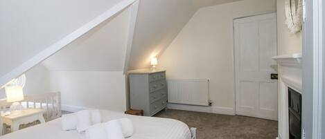 A bedroom with a bed, a dresser, a radiator, and a fireplace.