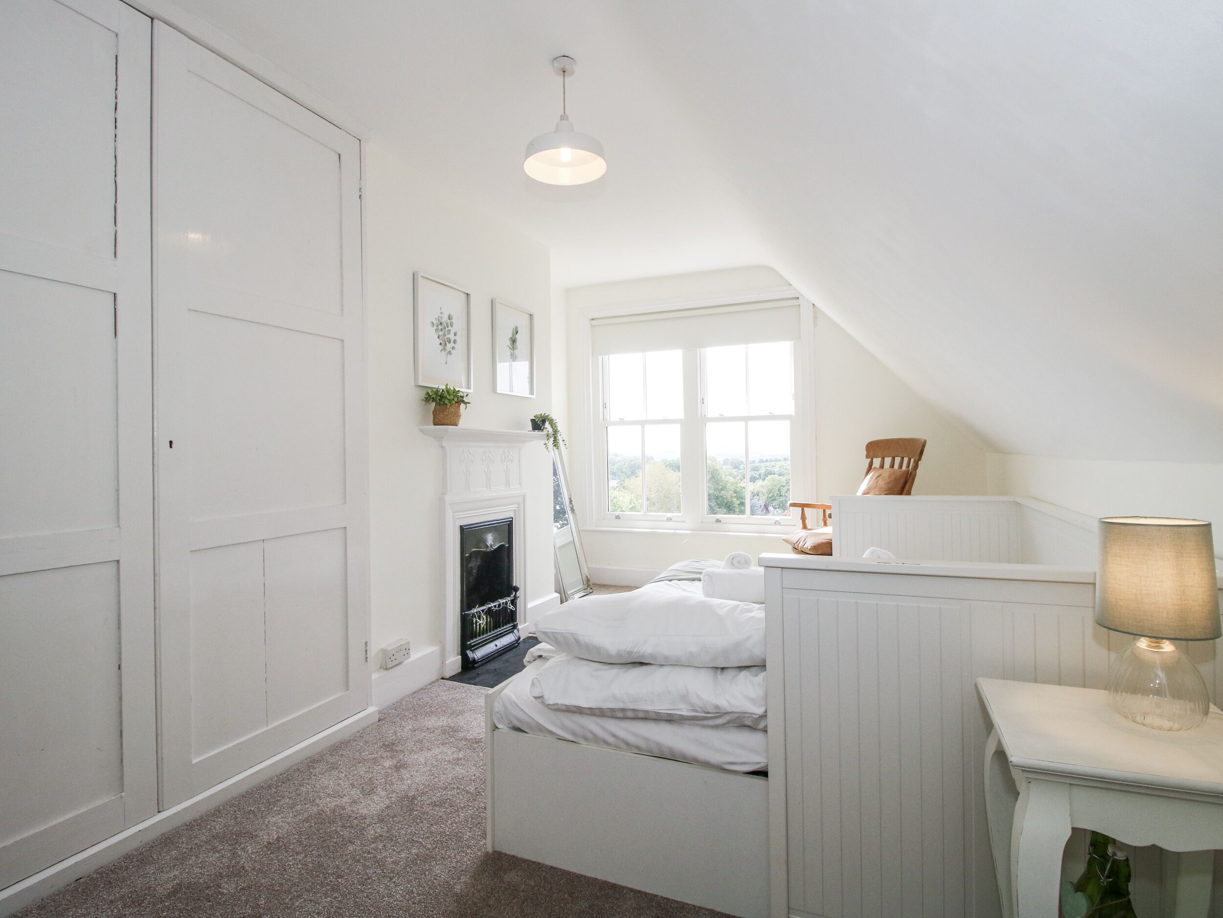 A bedroom with a bed, a nightstand, a lamp, a window, and a fireplace.