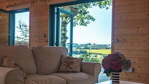 A wooden interior with a beige sofa, a white table, and a vase with flowers. - Owl Lodge (Liskeard)