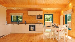 A wooden cabin with a kitchen area, dining table, and chairs. - Owl Lodge (Liskeard)