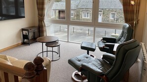 A room with a large arched window, a leather sofa, a small round table, and a flat-screen TV mounted on the wall. - The Clocktower (Perth)