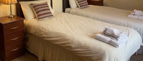 Two neatly made beds with white linens, striped pillows, and matching nightstands with lamps.