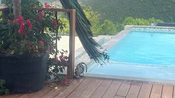 Eine Holzterrasse mit einer Pfauenstatue, einem Pool und Blick auf Hügel.