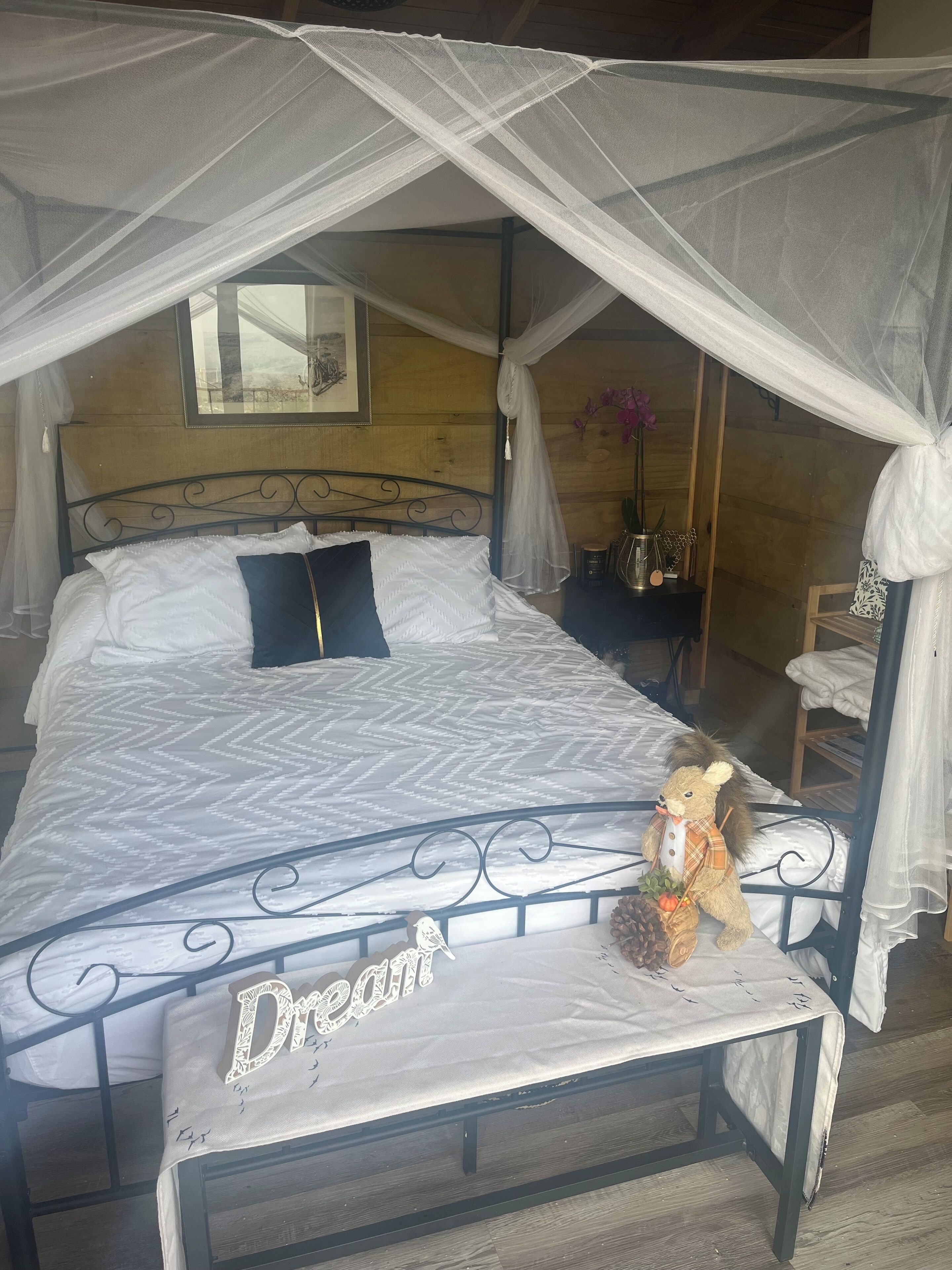 Un lit à baldaquin, un ours en peluche et une table de chevet ornée d’un vase de fleurs.