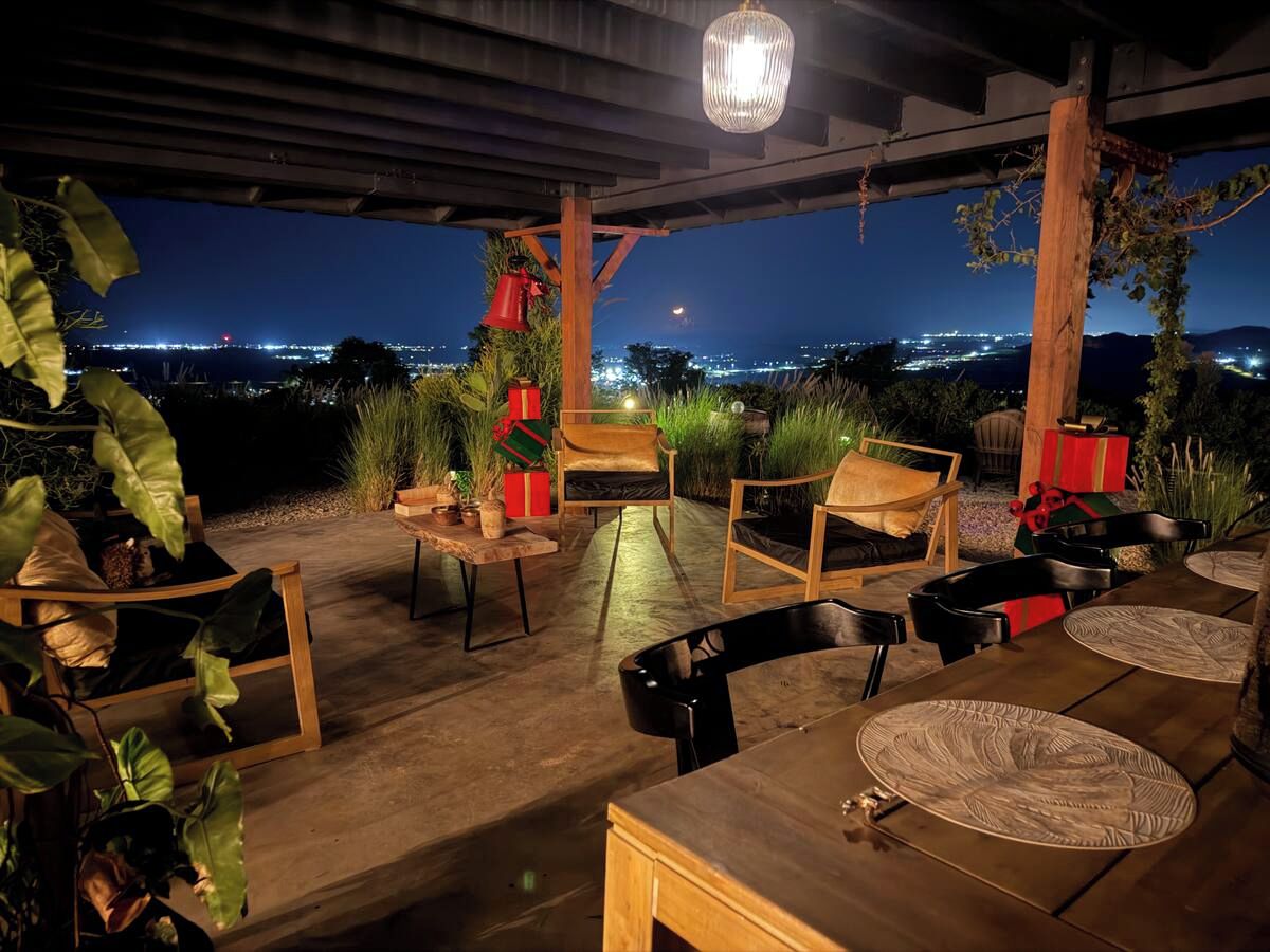 Un espacio al aire libre con mobiliario de madera y individuales tejidos, con vistas a un paisaje urbano nocturno.