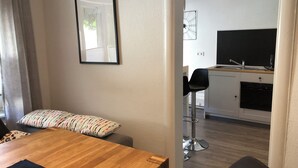 Una cocina moderna con encimera negra y electrodomésticos de acero inoxidable, un comedor con mesa de madera y sillas negras, y un cuadro en la pared.