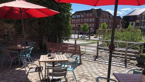 Un patio al aire libre con mesas y sillas, sombrillas rojas y un muro de ladrillo.