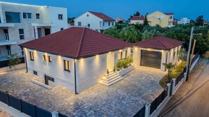 A modern two-story house with a red-tiled roof, a paved driveway, and a well-lit exterior. - Charming 3BR Villa with Heated Pool, Sauna and Gym (Privlaka)