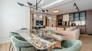 A modern living room with a marble dining table, green upholstered chairs, a beige sofa, and a kitchen area with wooden cabinets and a built-in oven. - Charming 3BR Villa with Heated Pool, Sauna and Gym (Privlaka)