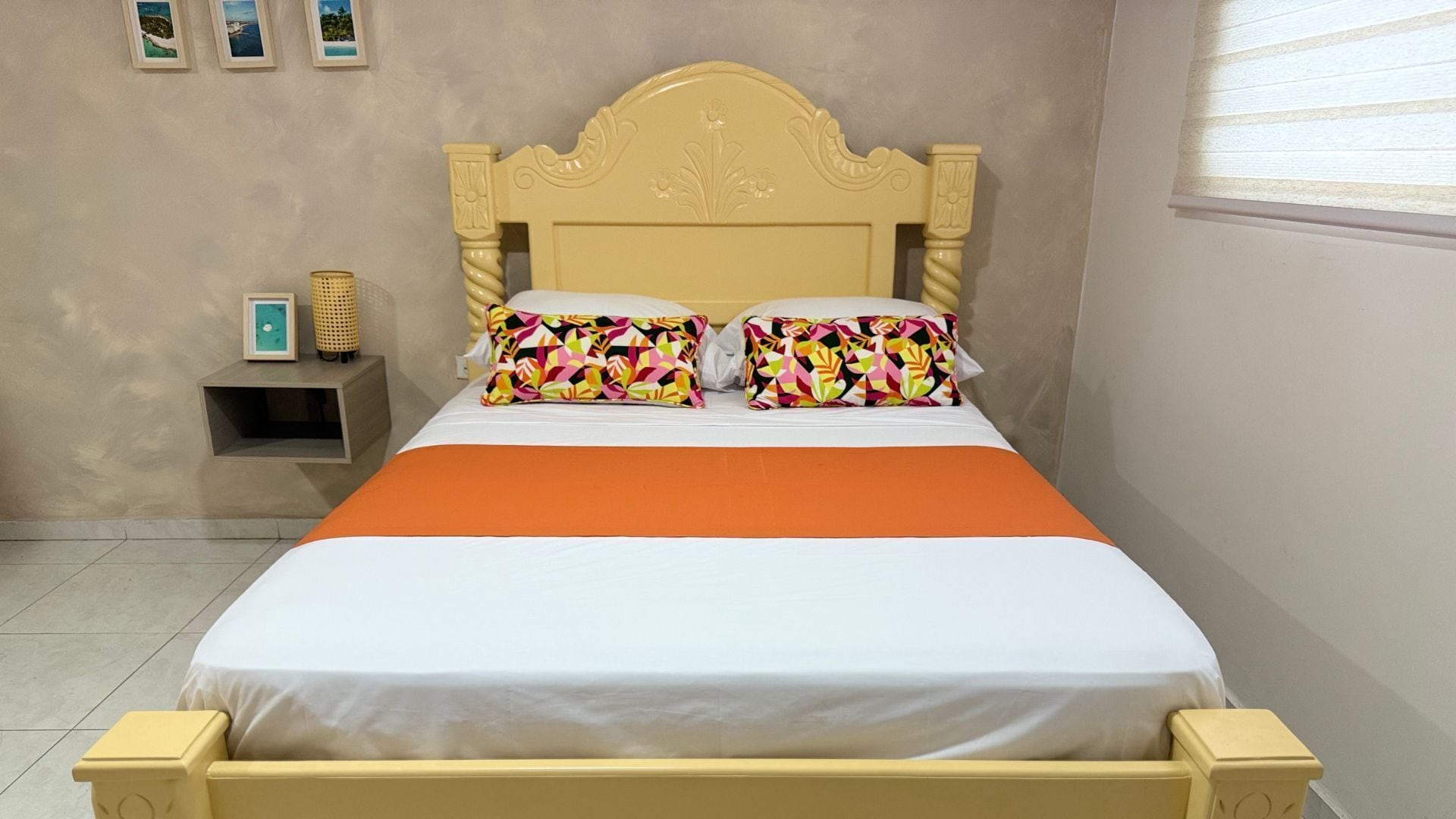 A bed with an orange bedspread, two pillows with a colorful geometric pattern, and a wooden headboard.