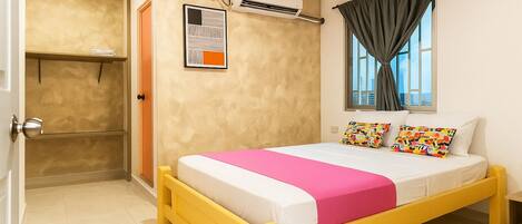A bedroom with a bed, a window with curtains, an air conditioning unit, and a door.