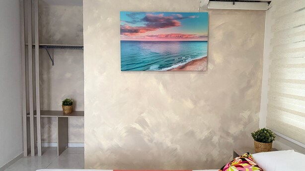A room with a large painting of a beach scene, a small plant on a shelf, and a colorful pillow on the bed. - Taybo House By St Hoteles (San Andrés)