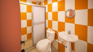 A bathroom with a white toilet, a sink, and a shower with a glass door. The walls are tiled in a checkered pattern of orange and white. - Taybo House By St Hoteles (San Andrés)