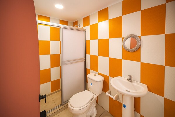 A bathroom with a white toilet, a sink, and a shower with a glass door. The walls are tiled in a checkered pattern of orange and white.