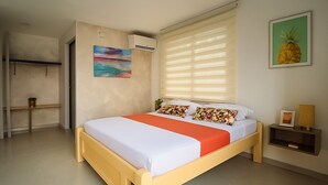 A bedroom with a bed, a nightstand, a wall-mounted air conditioner, a window with blinds, a painting, and a framed picture on the wall. - Taybo House By St Hoteles (San Andrés)