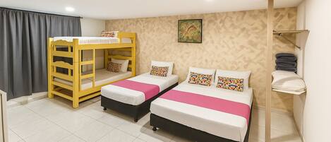 A hotel room with two beds, a bunk bed, a shower area, and a towel rack.