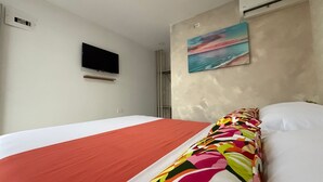 A hotel room with a bed, a TV mounted on the wall, and a painting above the bed. - Taybo House By St Hoteles (San Andrés)