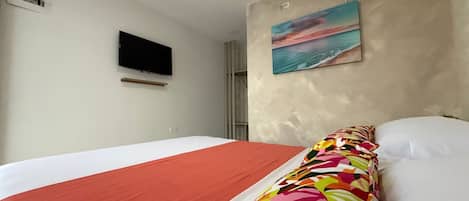A hotel room with a bed, a TV mounted on the wall, and a painting above the bed.