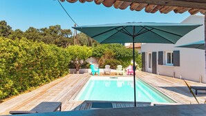A wooden deck with a swimming pool, outdoor chairs, and a large umbrella. - Villa Meia Di Porto-Vecchio (PORTO VECCHIO)
