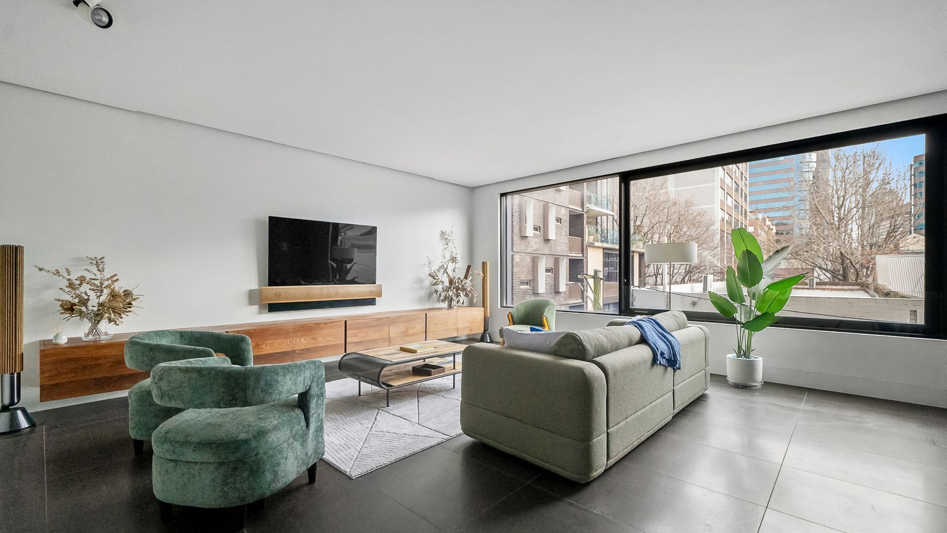 A modern living room with a large window, a flat-screen TV, and a sofa.