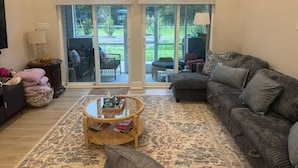 A living room with a sofa, a coffee table, and a rug. There is a window with blinds and a view of the outdoors.