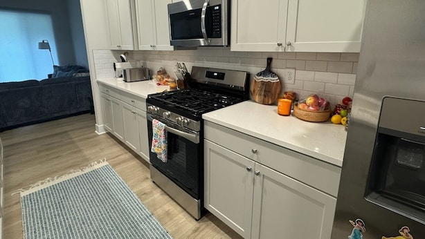 A modern kitchen with white cabinets, stainless steel appliances, and a wooden floor.