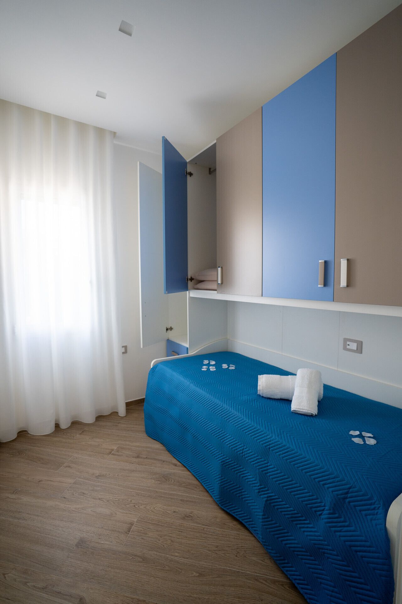 A hotel room with a bed, a wardrobe, and a window with curtains.