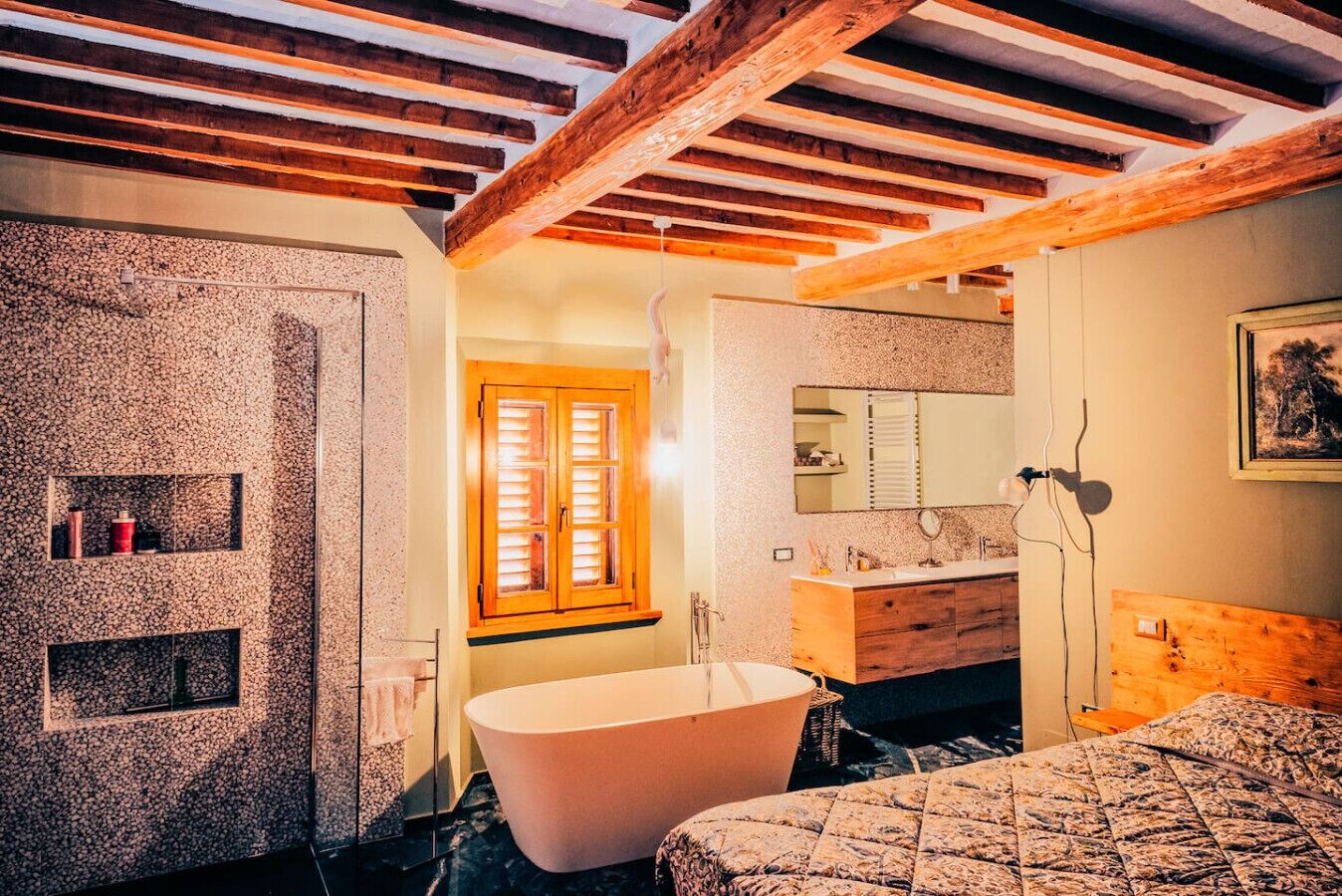 Une salle de bain avec une baignoire sur pieds, des poutres en bois, une fenêtre avec volets et un miroir au-dessus du lavabo.
