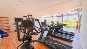 A gym with cardio equipment, a TV, and a large window with a view of a garden. - Flat Île de Pipa Taiti - By Almare (Tibau do Sul)
