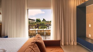 A modern hotel room with a large bed, a seating area with a view of a balcony, and a built-in TV shelf. - Flat Île de Pipa Taiti - By Almare (Tibau do Sul)
