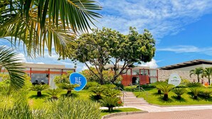 A modern hotel with a well-maintained garden, a clear sky, and a sign for 'ILE de Pipa'. - Flat Île de Pipa Taiti - By Almare (Tibau do Sul)