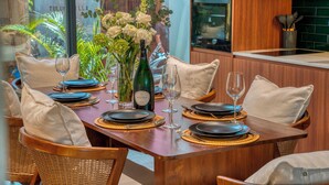 A dining area with a wooden table set for four, surrounded by wicker chairs with cushions.