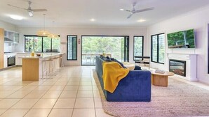 A spacious living area with a sofa, a coffee table, and a fireplace. There is a kitchen with a bar area and large windows. - 24 Nautilus - Tangalooma - Moreton Island (moreton island)
