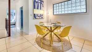 A dining area with a glass table and yellow chairs, a large abstract painting, and a window with frosted glass panels. - 24 Nautilus - Tangalooma - Moreton Island (moreton island)