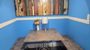 A corner room with a blue wall, a rustic wooden table with a white lamp, and a decorative painting above. - 🍒CHERRY’S DELIGHT - Where timeless comfort is served with a cherry on top! (Glasgow)