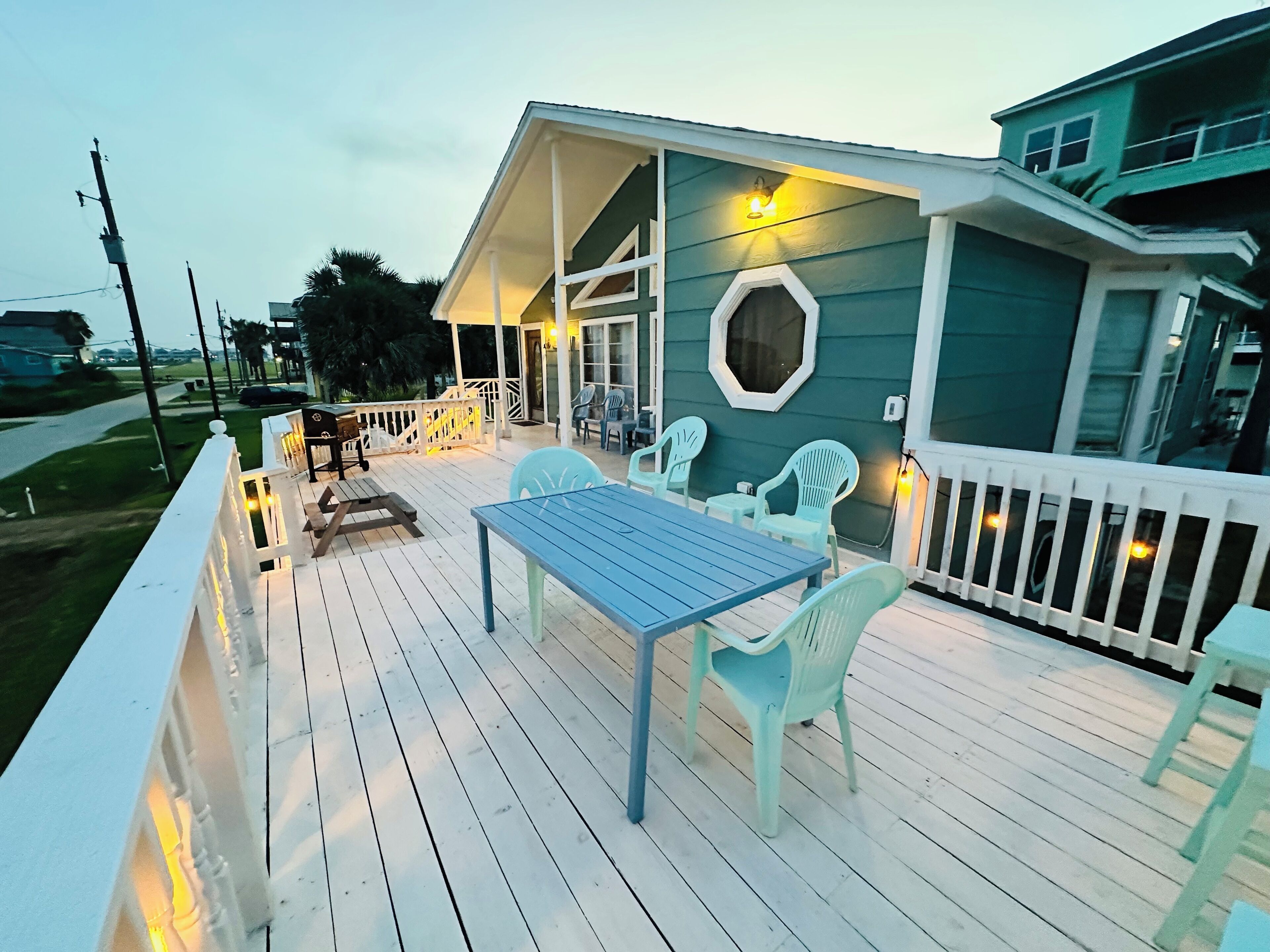 Eine Terrasse mit Tisch und Stühlen, ein überdachter Bereich mit Geländer und ein Gebäude mit grüner Fassade.