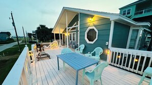 A deck with a table and chairs, a covered area with a railing, and a building with a green exterior. - Beachside Get-A-Way! Walk to the Beach! (Galveston)