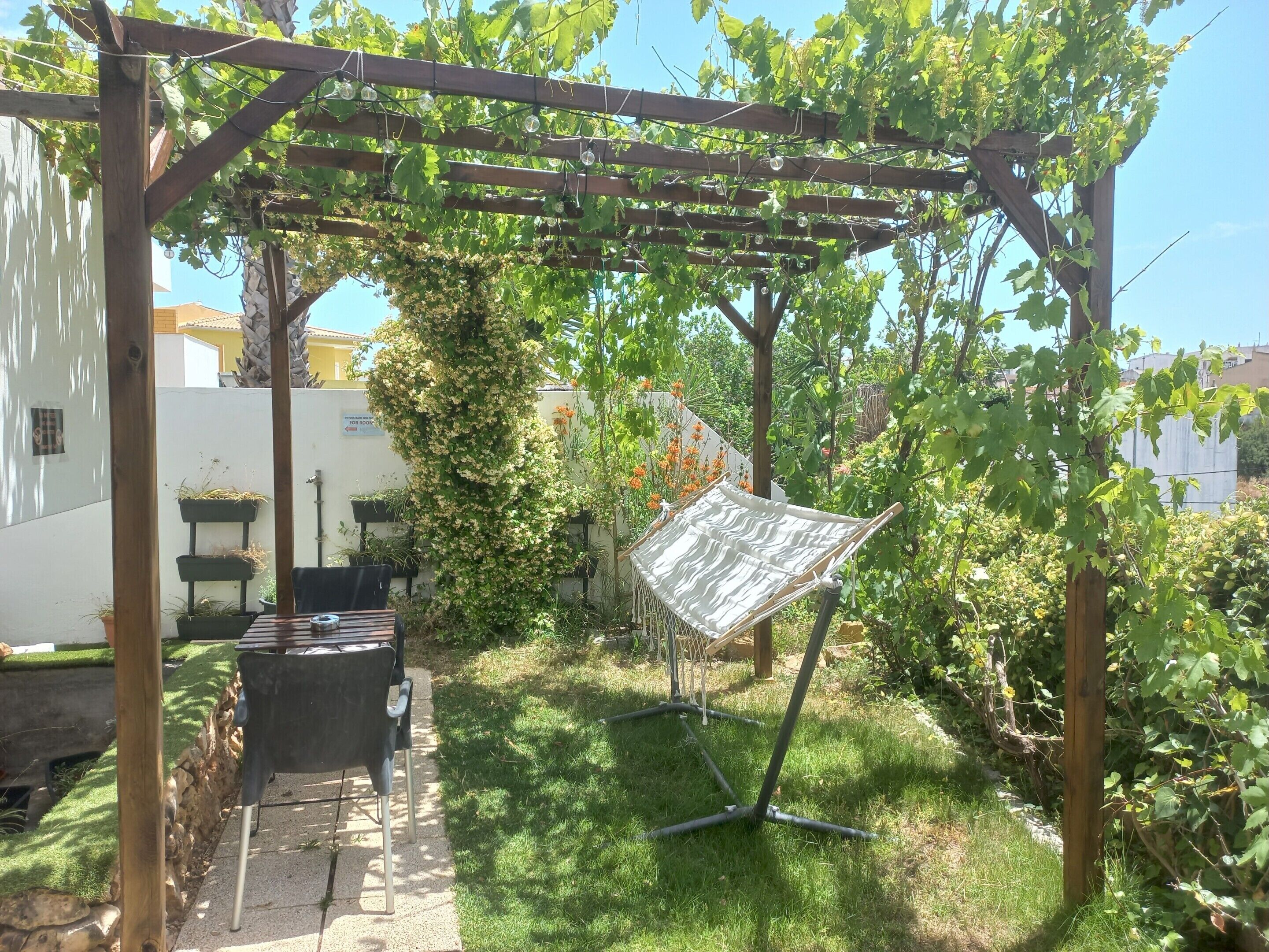 Un jardín con una pérgola, una hamaca y una zona de barbacoa.