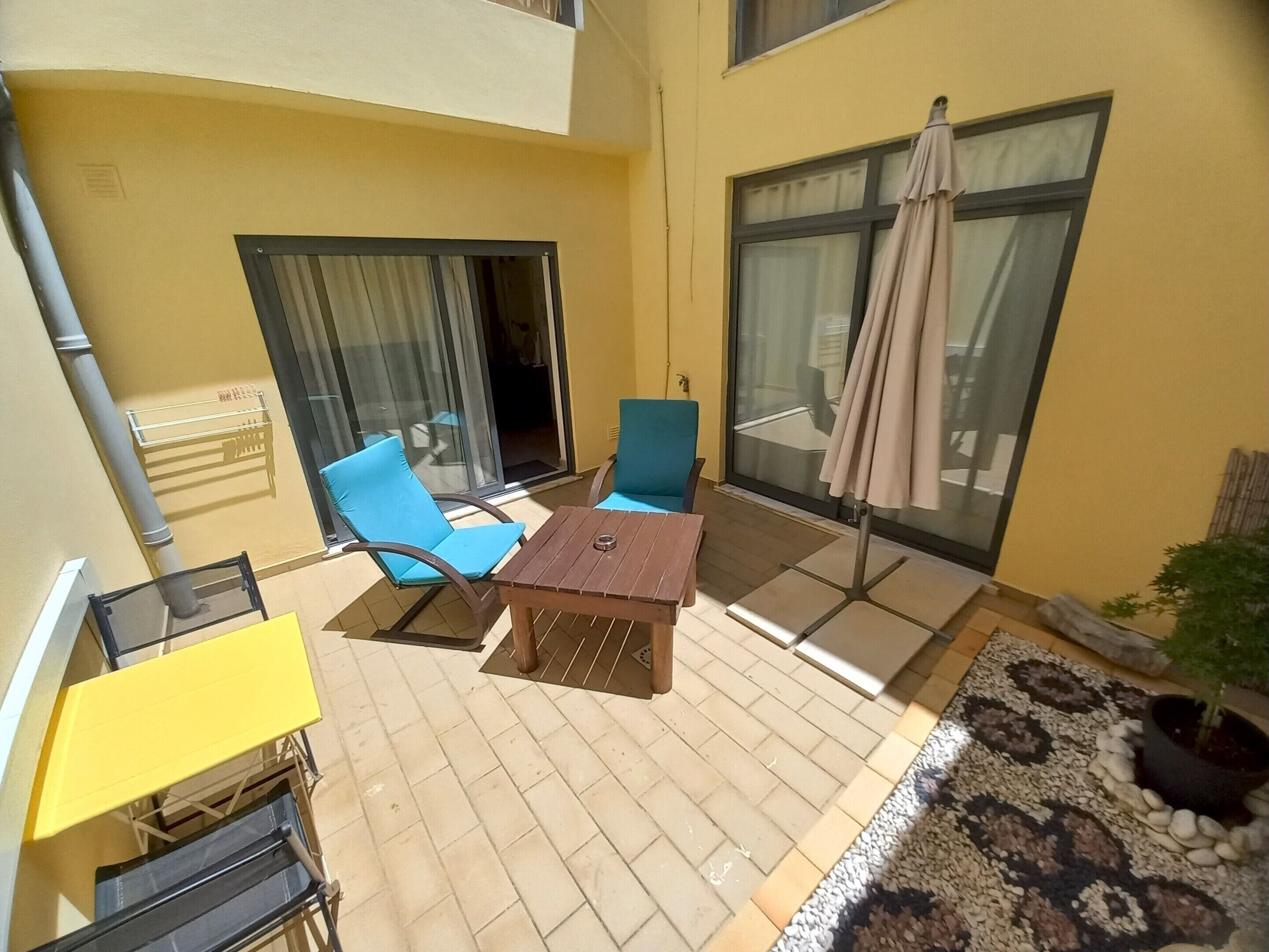 A balcony with a table and chairs, a potted plant, and a view of the street.