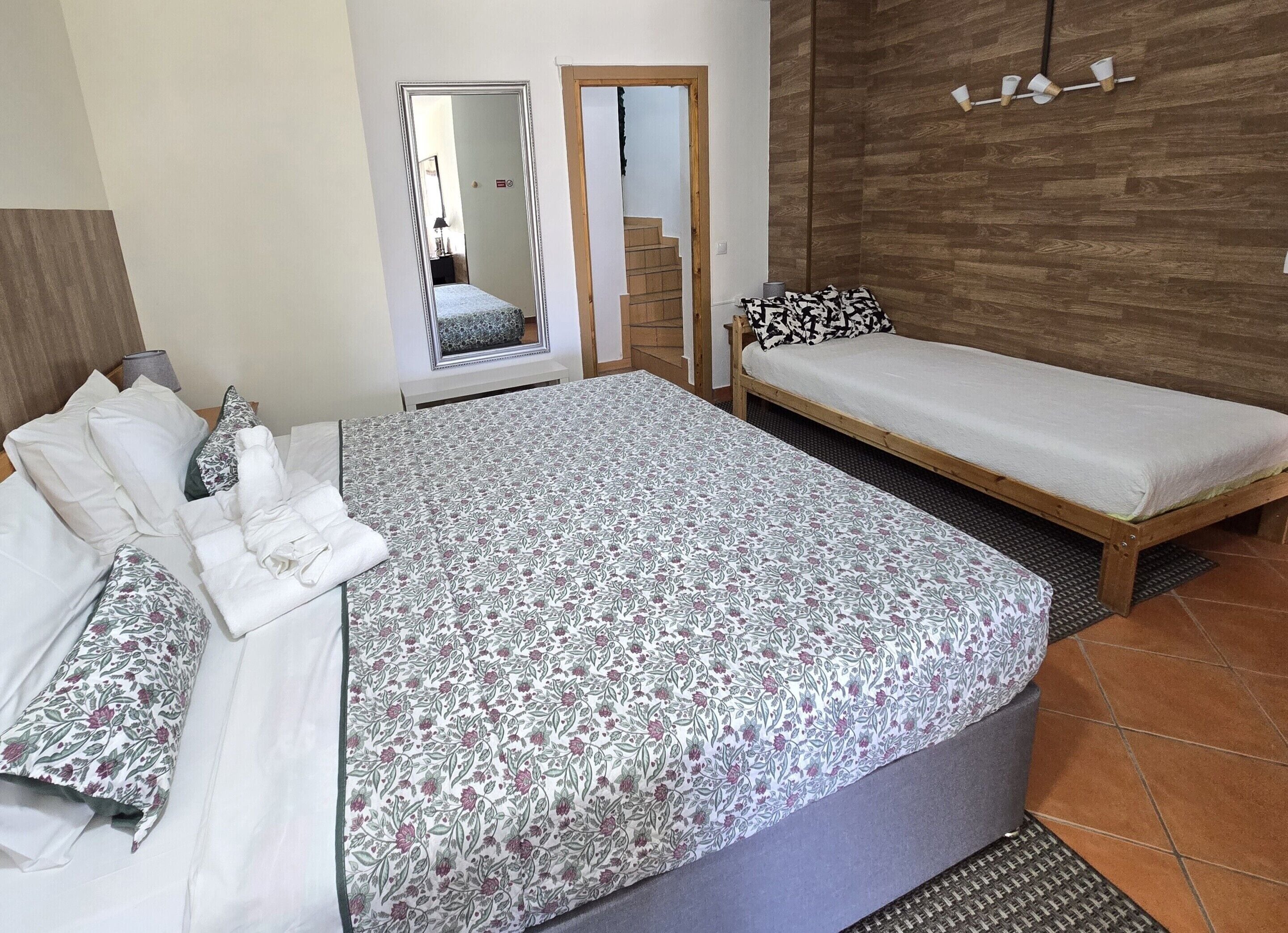Ein Schlafzimmer mit einem großen Bett, einem kleineren Bett, einem Spiegel, einer Holzverkleidung und einem kleinen Tisch mit einer Lampe.