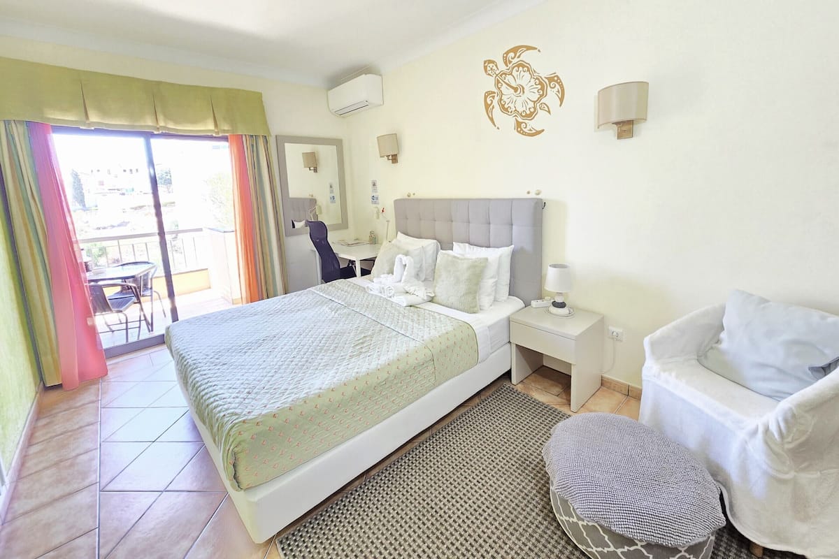 A hotel room with a bed, bedside tables, a chair, a desk, and a balcony with curtains.