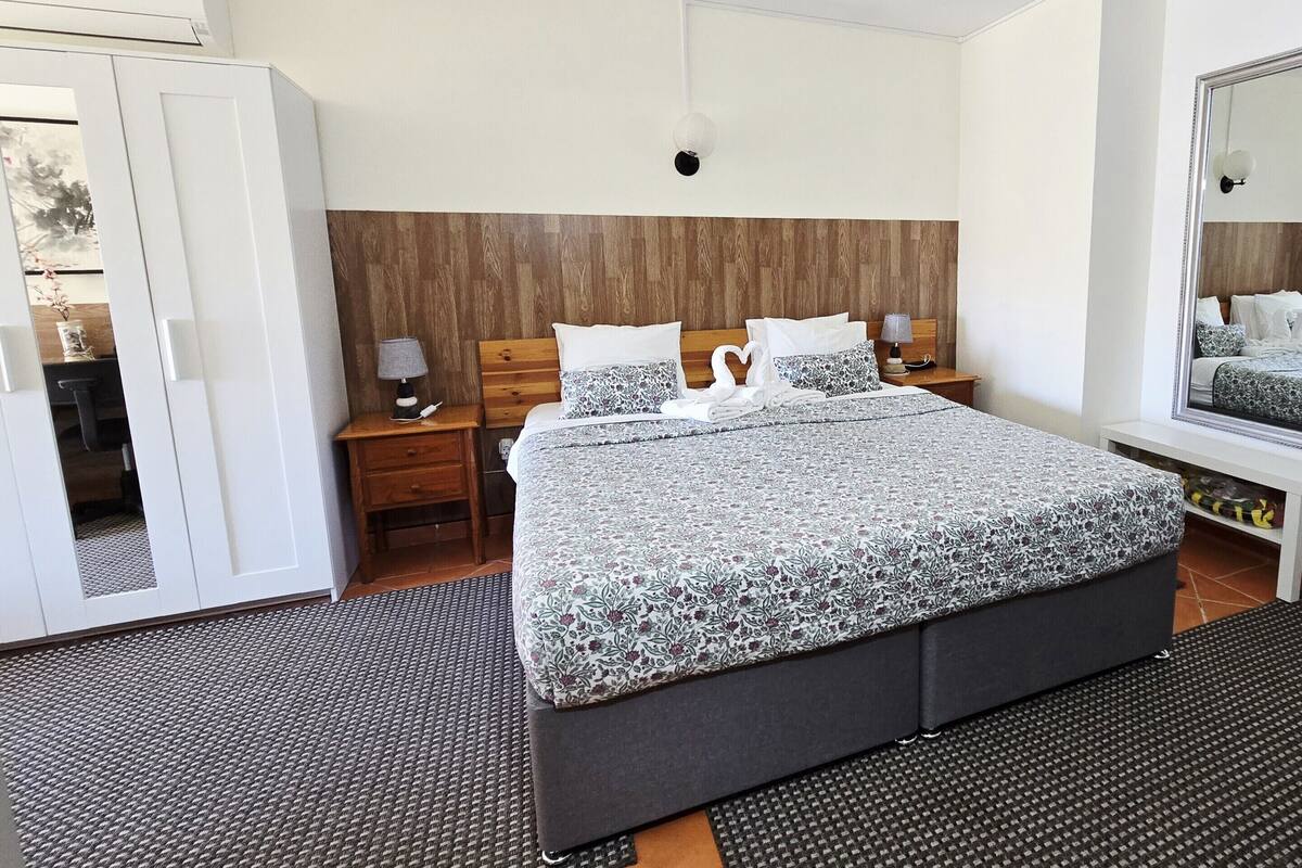 A bedroom with a large bed, wooden headboard, two bedside tables with lamps, a wardrobe, and a mirror.