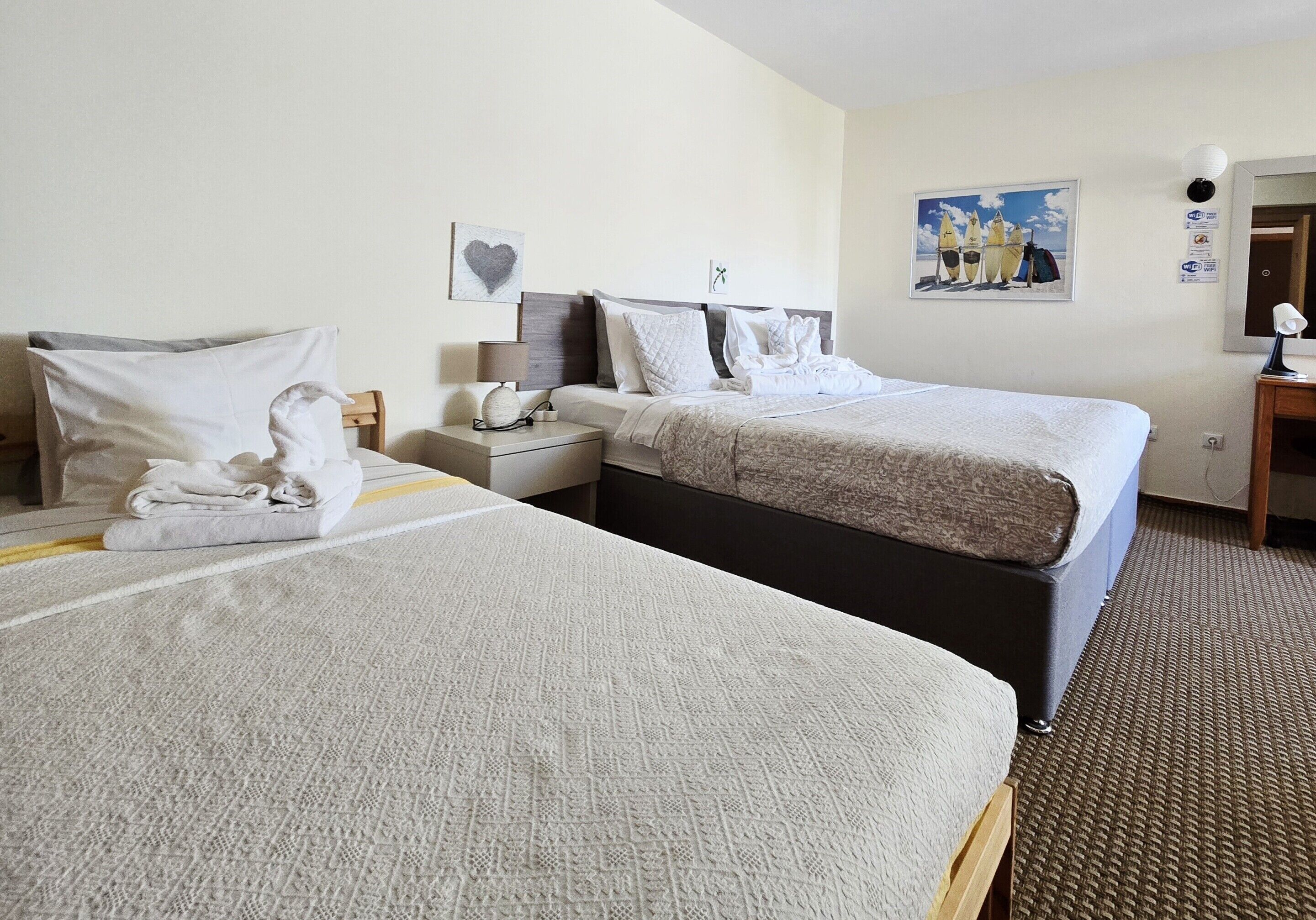 A hotel room with two beds, a nightstand, a lamp, and a painting on the wall.