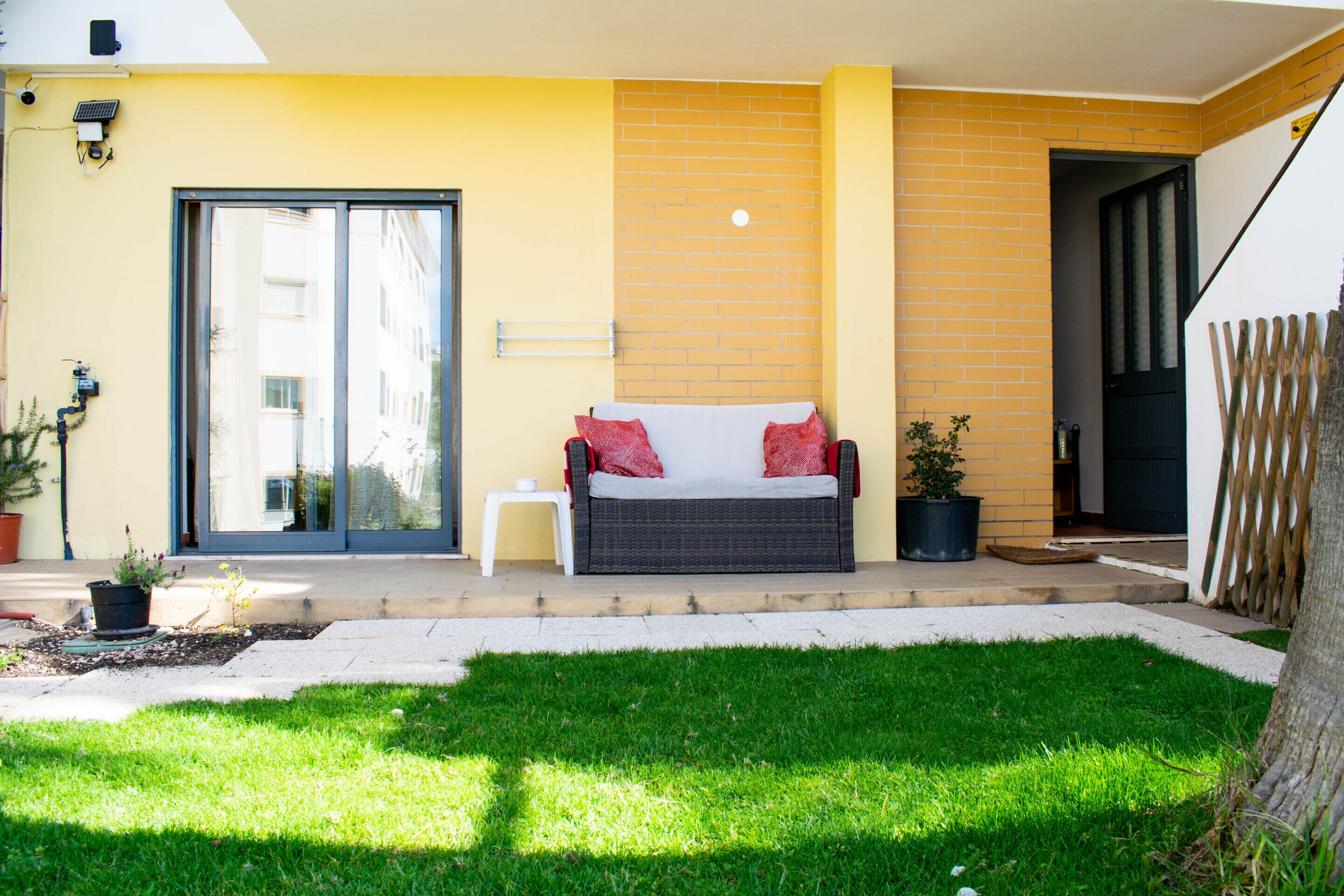 A patio with a wicker sofa, a small table, and a potted plant.